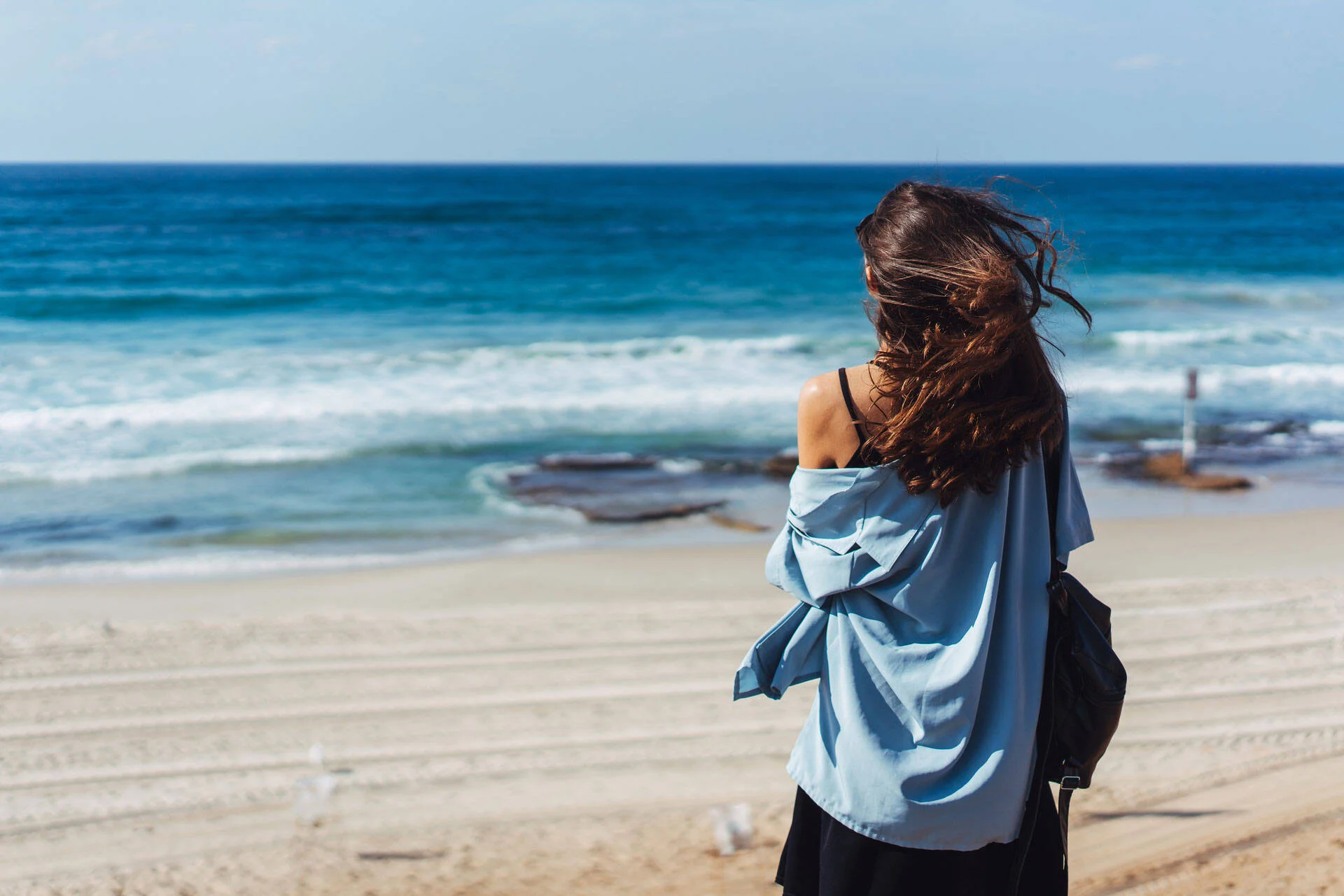 Woman standing on a beach looking out at the ocean